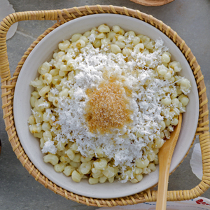 Binatog in a serving plate topped with grated mature coconut and brown sugar.