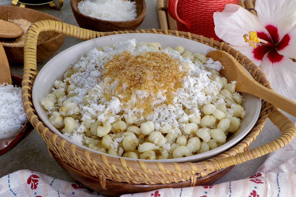 Binatog in a serving plate topped with grated mature coconut and brown sugar.