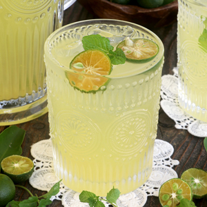 Calamansi juice in a glass served over ice with calamansi slices and mint leaves.