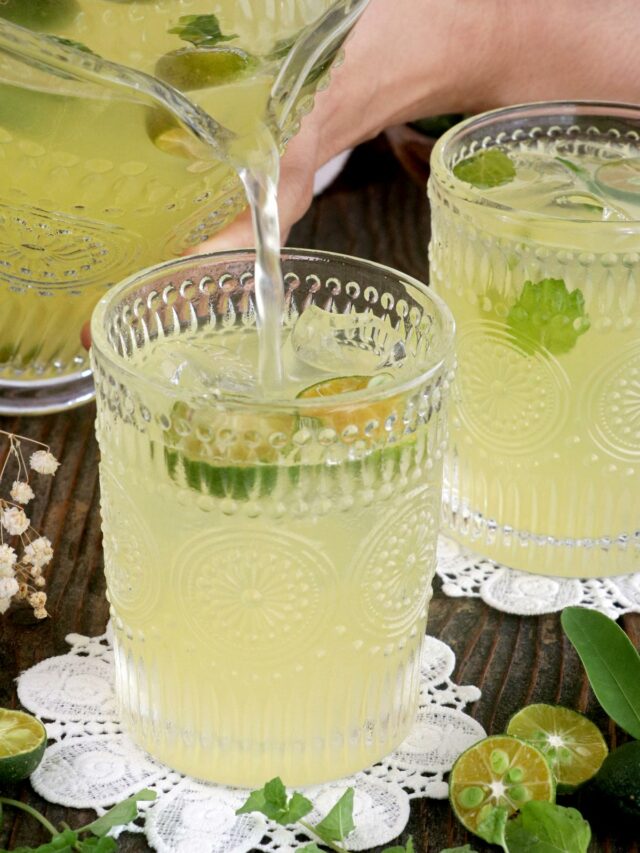 Fresh calamansi juice being poured in a glass with ice, calamondin slices, and mint leaves.