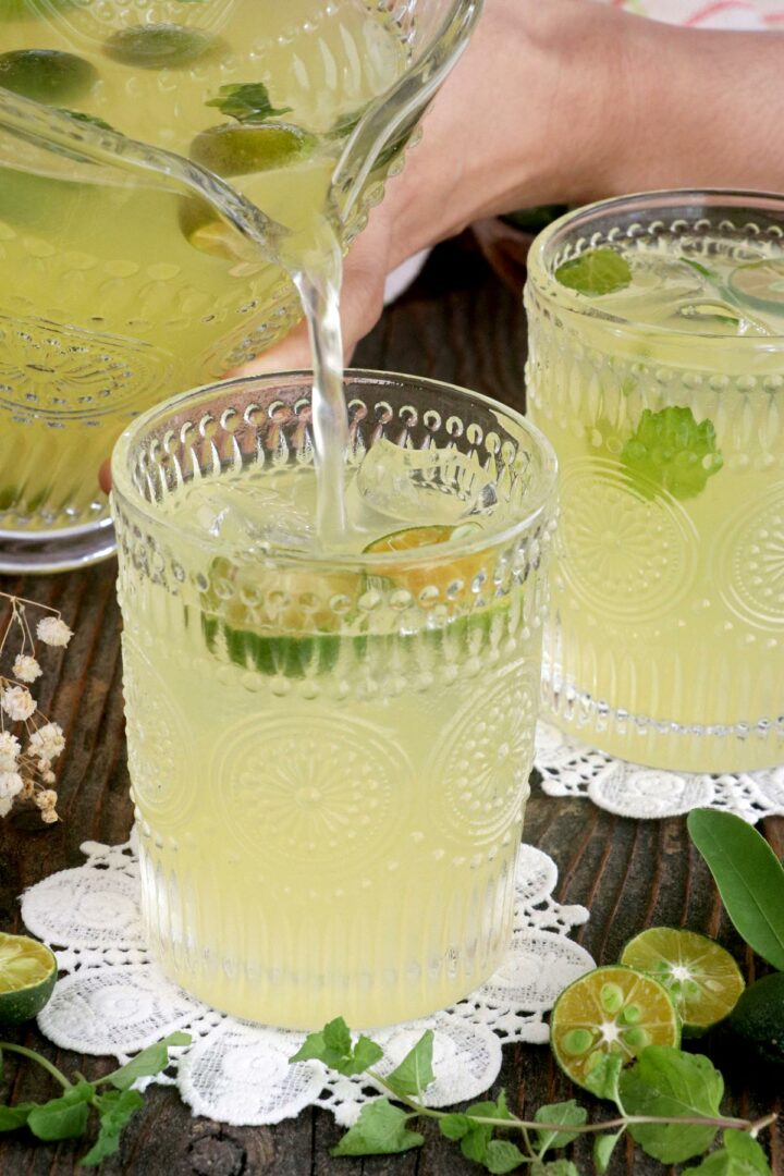 Fresh calamansi juice being poured in a glass with ice, calamondin slices, and mint leaves.