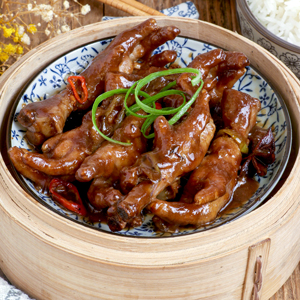 Chicken Feet Dimsum in a bamboo steamer with Thai chilis and star anise. garnished with spring onion.