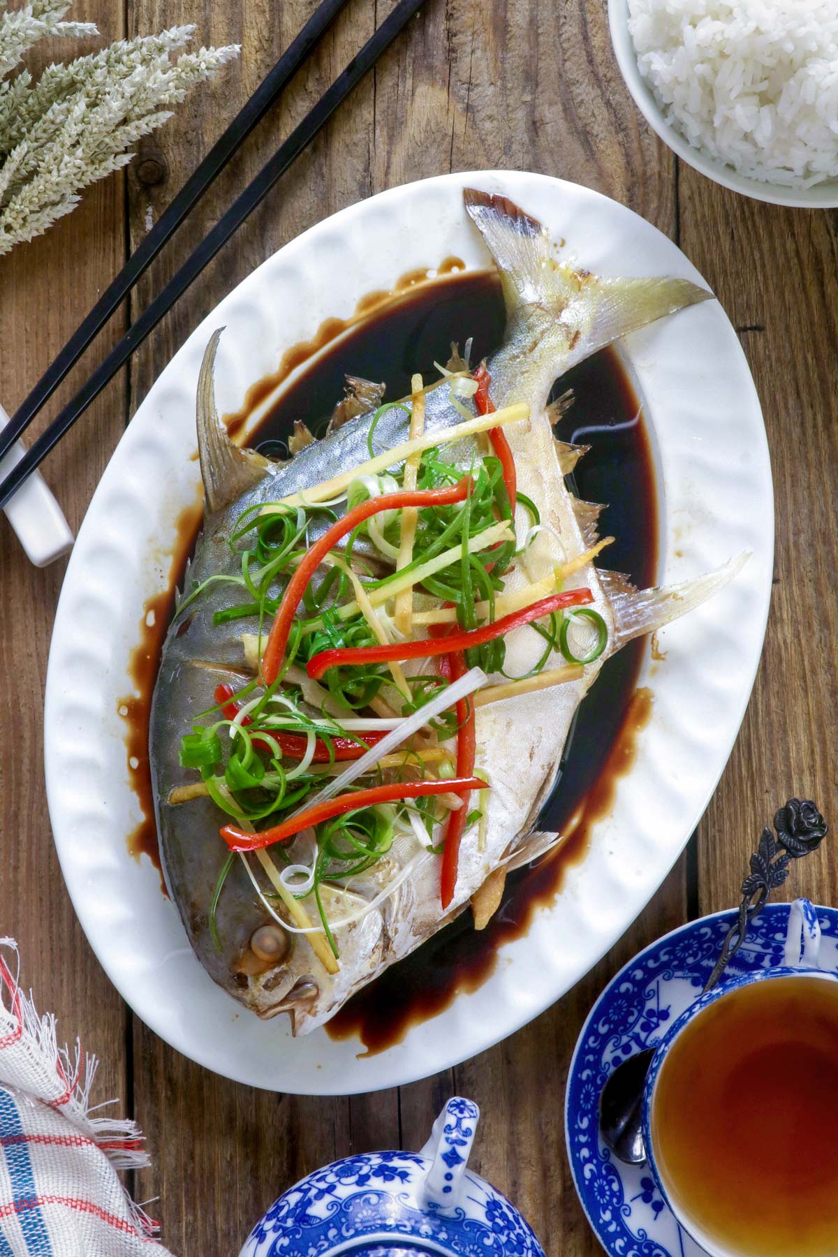 Steamed pompano fish Chinese- style in a serving platter with sliced ginger, green onions, and cilantro on top.