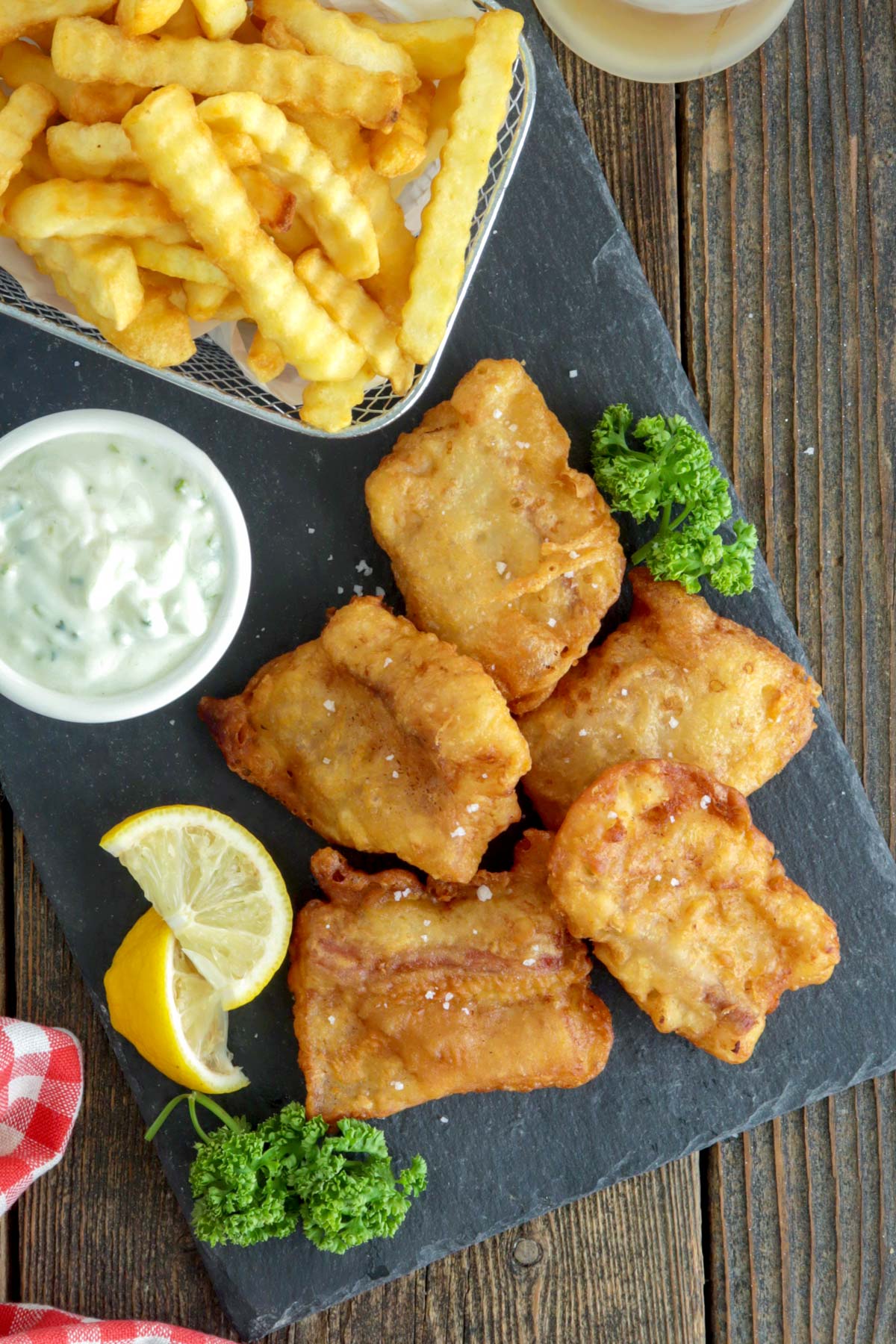 Crispy beer battered fish served with dipping sauce, fries, and lemon wedges.