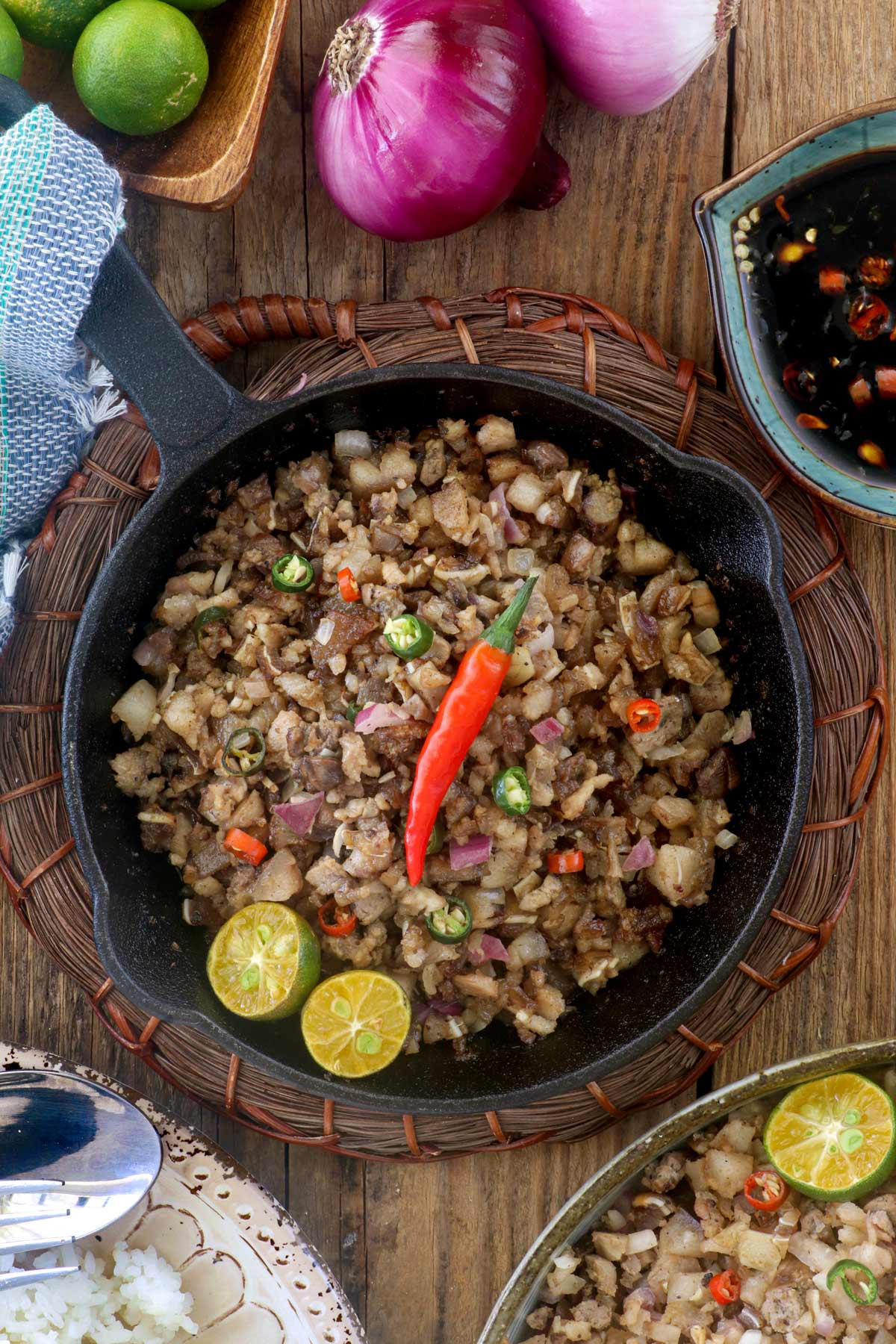 Authentic Sisig in a sizzling pan with calamansi wedges and chili.