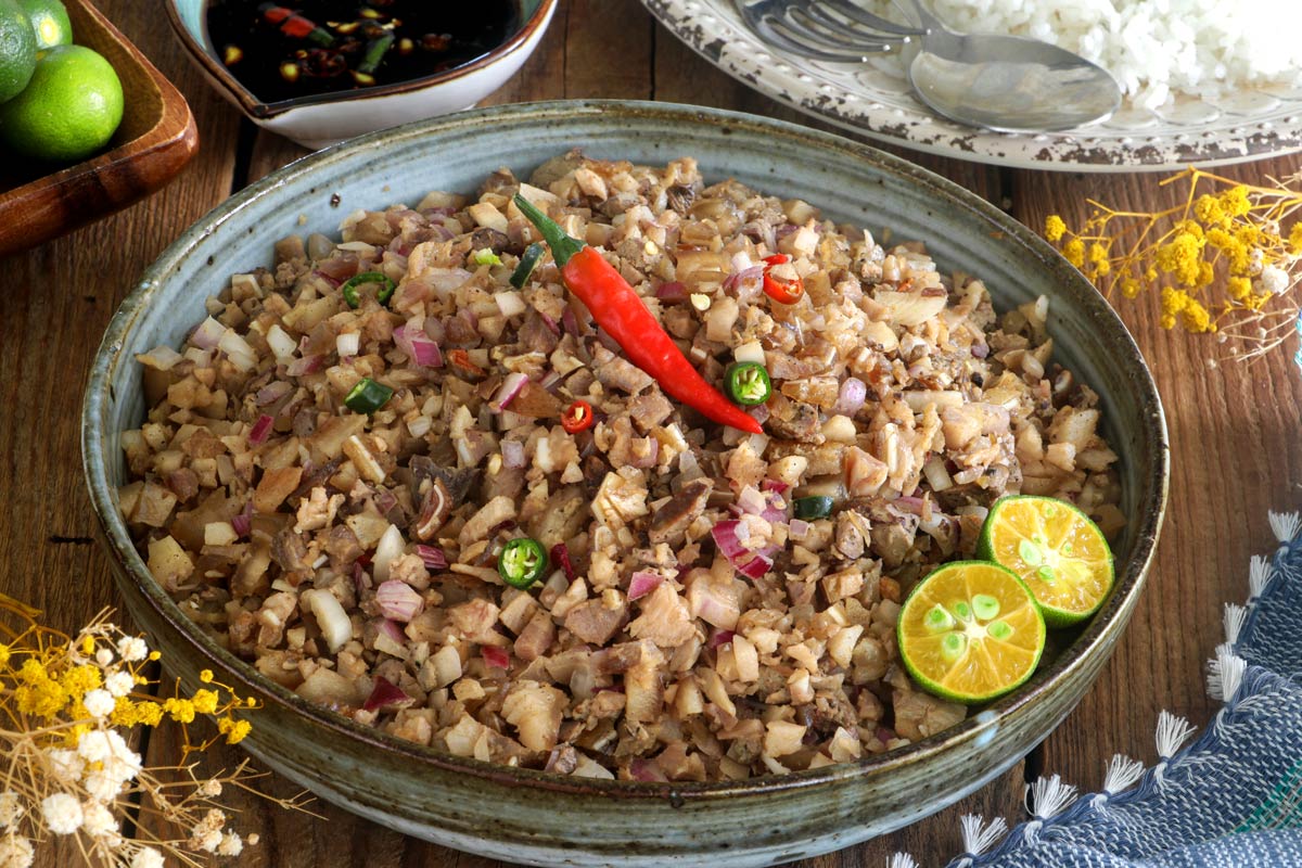 Authentic sisig in a serving plate served with rice and dipping sauce.