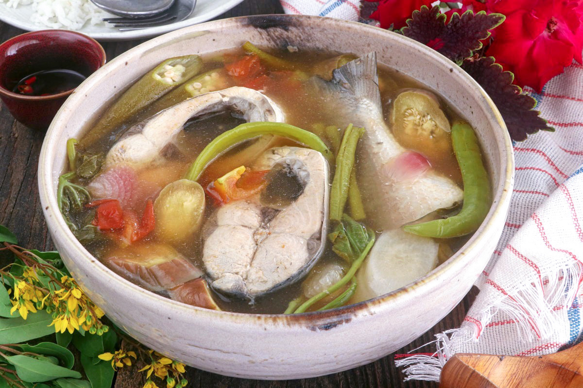 A bowl of sinigang na bangus with slices of milkfish, kangkong, eggplant, radish, and chilis.