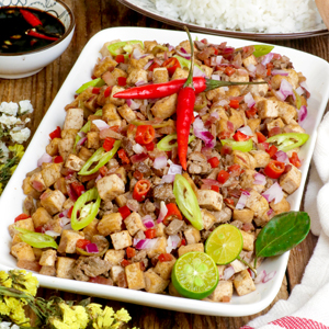 Tofu Sisig on a serving plate with sliced calamansi and red chili served with rice and cold beer.