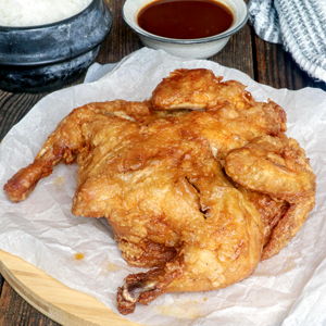 Super crispy whole fried chicken on a serving plate served with dipping sauce and rice.