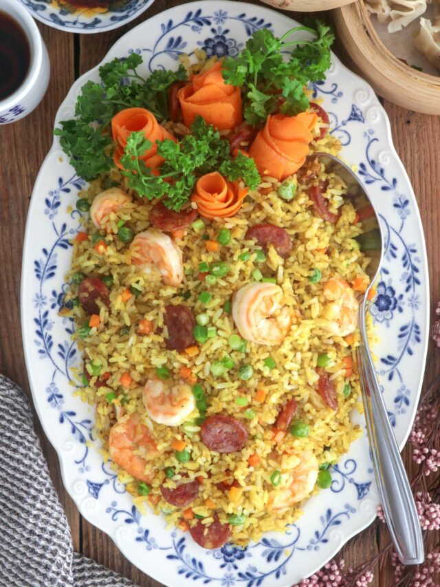 Yang Chow fried rice in a serving platter loaded with shrimp, sausages, eggs, carrots, and green peas.