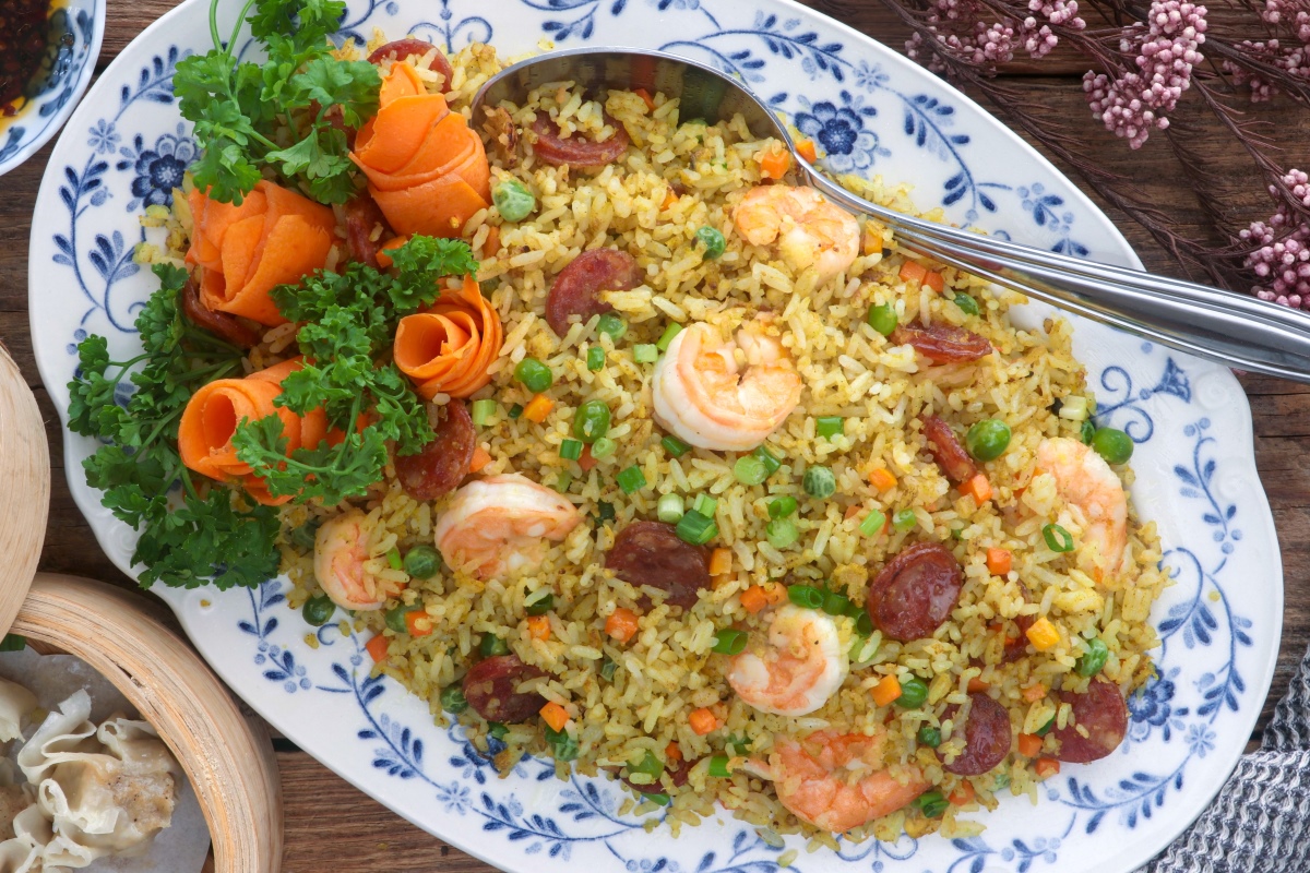 Yang Chow fried rice in a serving platter loaded with shrimp, sausages, eggs, carrots, and green peas.